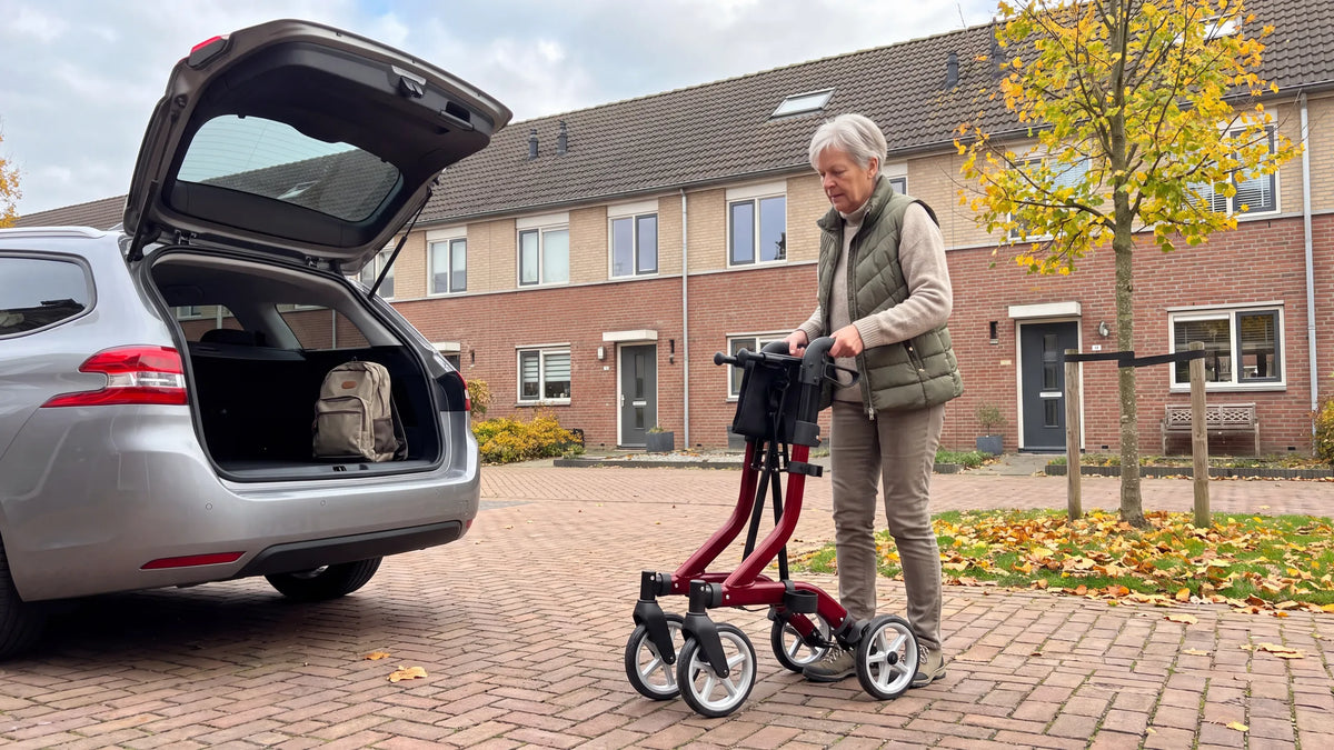 Folded Parvum SuperLight Plus in red next to the open trunk; a woman takes it by the handles.