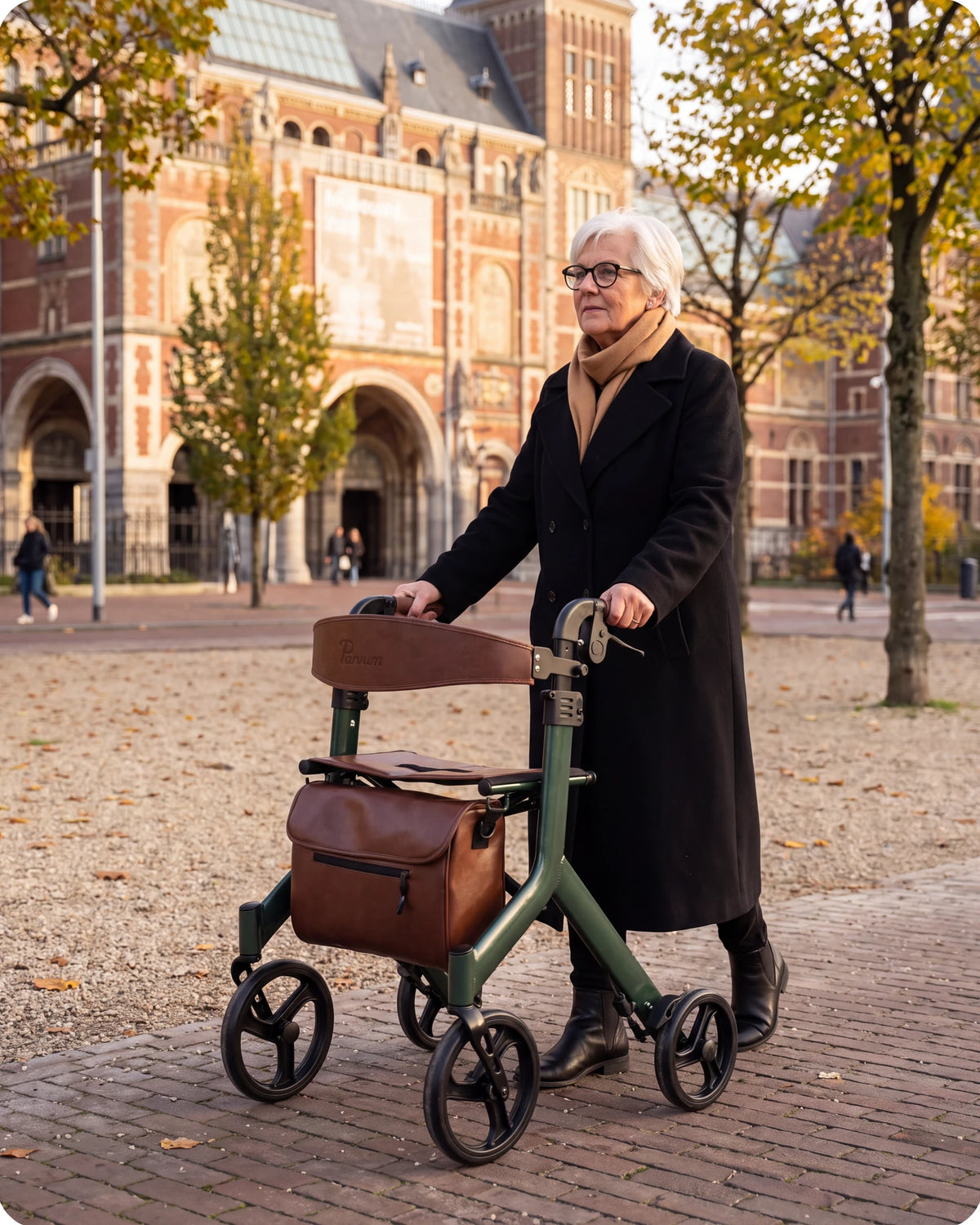Parvum Vesta in moss green on a museum square; a woman in a black coat walks with the rollator.